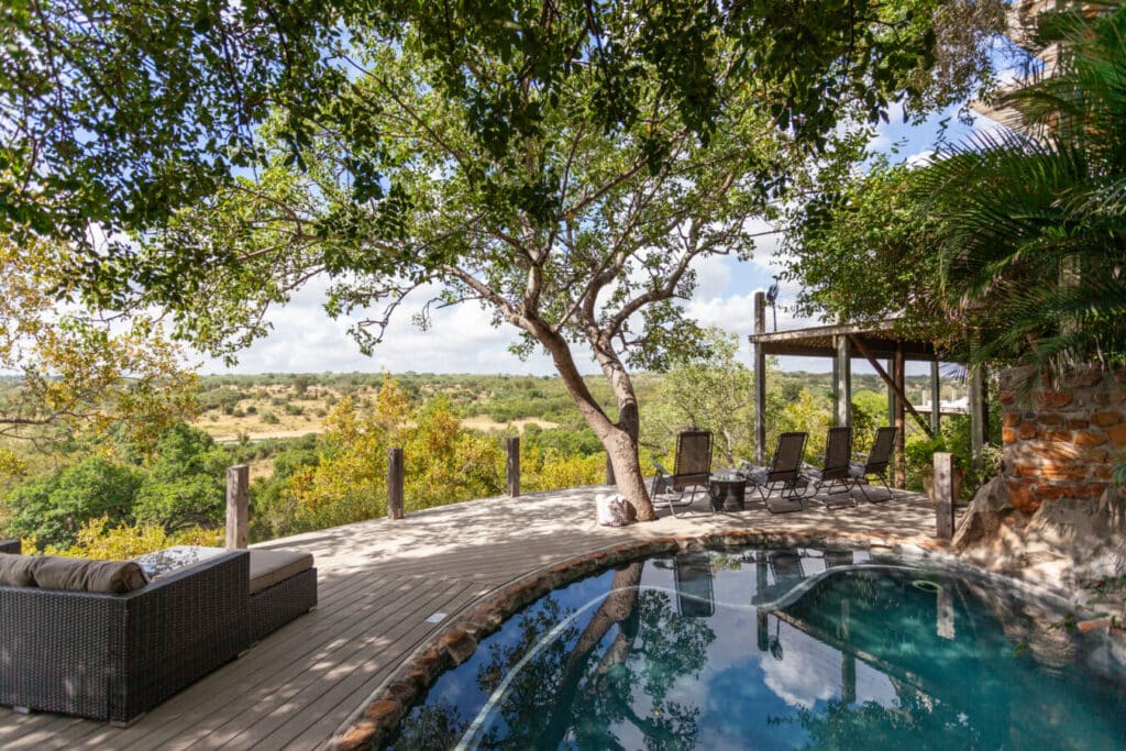 Outdoor patio with a curved pool, lounge chairs, and a shaded seating area overlooking a savannah-like landscape. It’s a tranquil retreat.