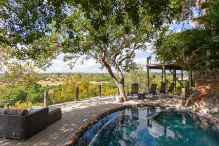Outdoor patio with a curved pool, lounge chairs, and a shaded seating area overlooking a savannah-like landscape. It’s a tranquil retreat.