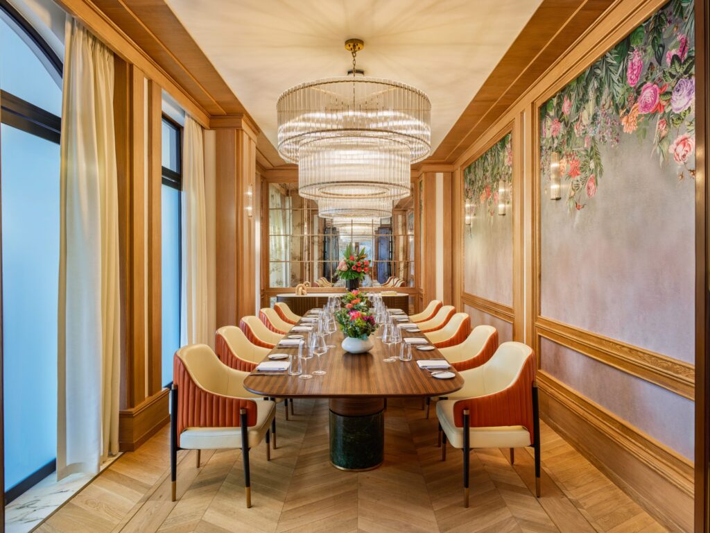 Elegant dining room with a long wooden table, cream and orange chairs, and a large crystal chandelier overhead