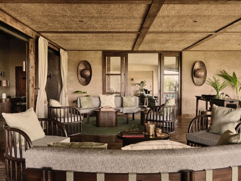 Open living area with a woven ceiling, wooden beams, and mid-century seating around coffee tables in earth tones and green accents.