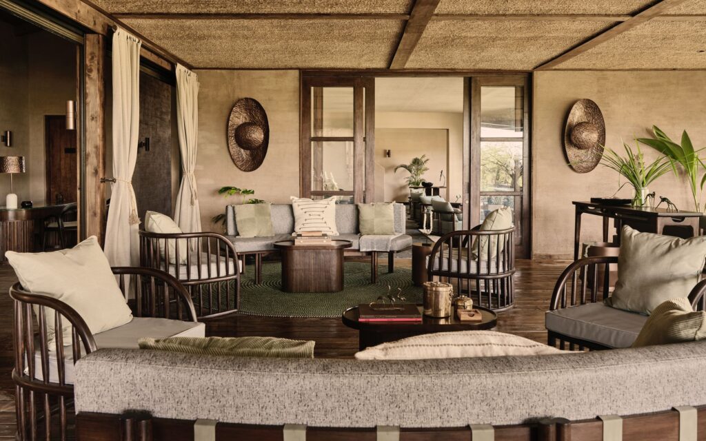 Cozy living room with neutral-toned sofas, round wooden coffee tables, and wicker chairs in a spacious lounge, plants and textured walls visible.