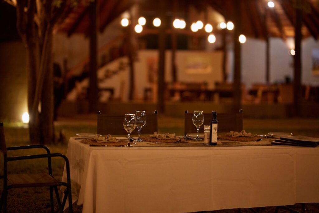 Outdoor dining table at night with wine glasses and a bottle, soft bokeh lights in the background.