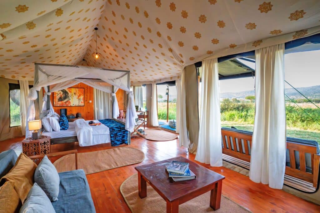 Luxurious safari tent bedroom with a four-poster bed, sheer curtains, warm pendant light, and open landscape outside