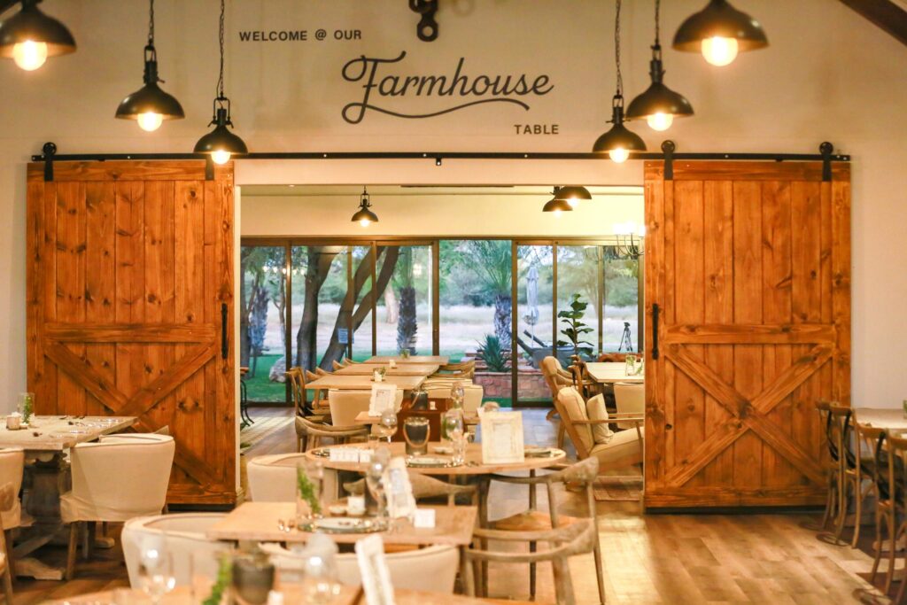 Rustic restaurant dining area with sliding wooden barn doors, dressed tables, and warm hanging lights.