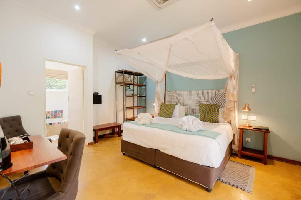Hotel bedroom featuring a white canopy bed with sheer drapes, green accent wall, and a wooden nightstand with a copper lamp.