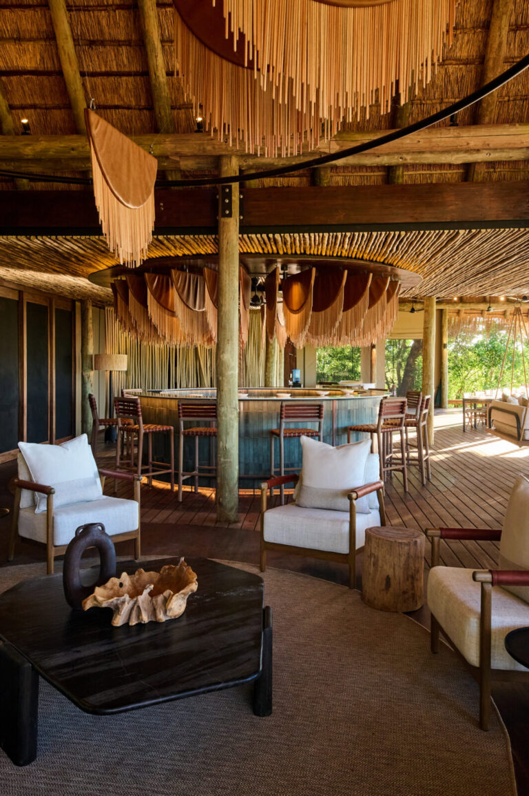 Open-air lounge with a circular bar under a thatched roof, surrounded by wooden posts and woven decor.