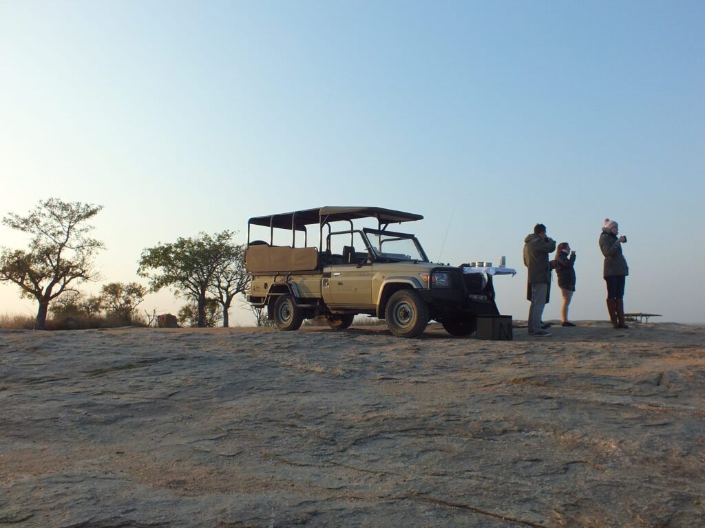 Group of four people standing on a sandy bluff, taking photos beside a beige open-top SUV with a canopy