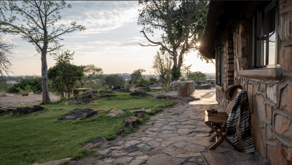 Stone cottage patio at sunset with a wooden chair draped in a striped blanket beside a stone wall.