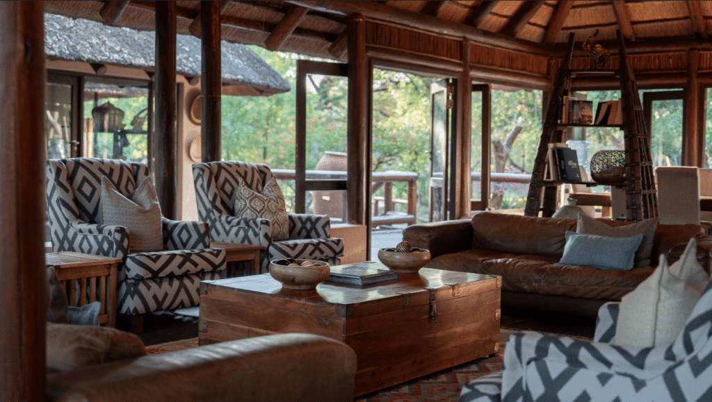 Cozy rustic living room with wooden beams, patterned armchairs, a brown leather sofa, and a wooden chest coffee table.