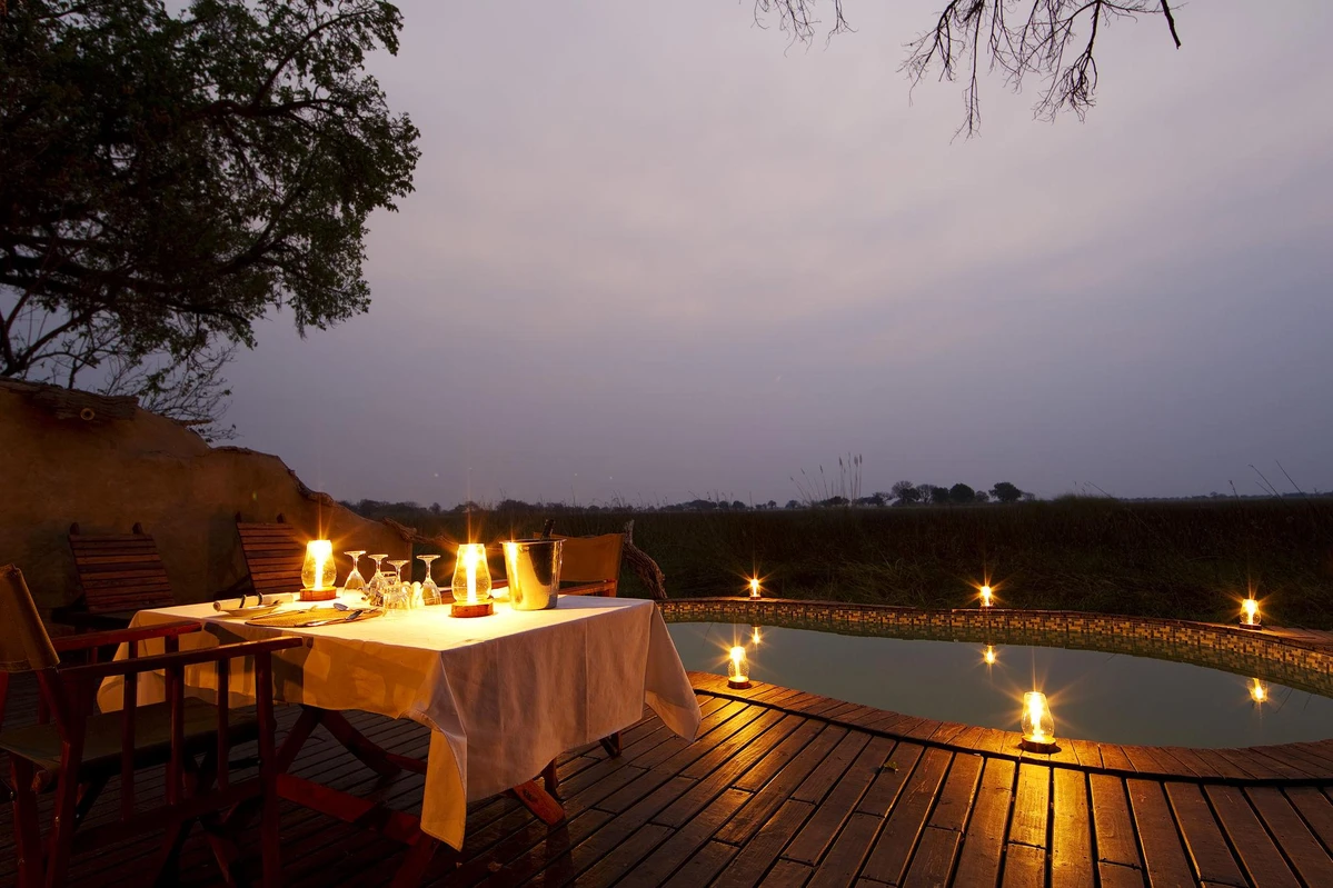 Outdoor candlelit dinner setup on a wooden deck beside a small pool at dusk/evening light.